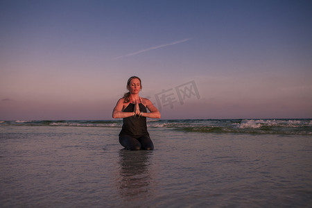 日落时分一名成熟女子在海滩上练习跪瑜伽姿势