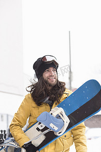 面带微笑的男性滑雪板运动员在街上扛着滑雪板