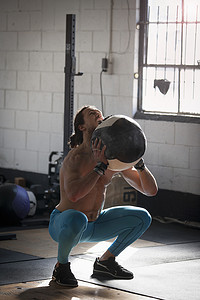 健身球摄影照片_一名男子在健身房里拿着药球蹲着