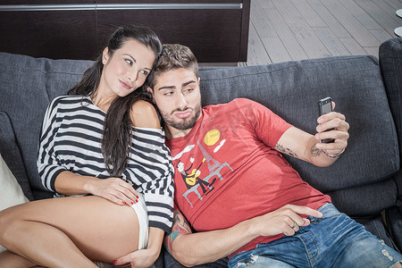 一对年轻夫妇在沙发上用智能手机自拍