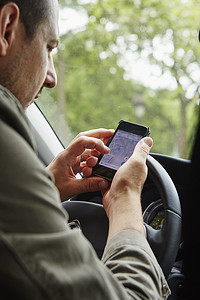 一名中年男子坐在车里在智能手机上看地图