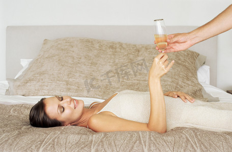 无酒精饮料摄影照片_躺在床上拿着香槟酒杯的女人