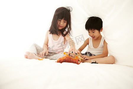 年轻的中国男孩和女孩在床上玩床单下的玩具