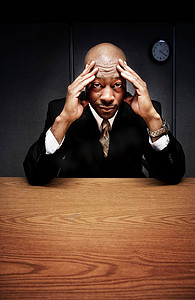 女性焦虑摄影照片_头顶双手坐在办公桌前的生意人