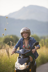 女子骑马摄影照片_快乐的年轻女子骑着轻便摩托车在乡村公路上行驶西班牙马略卡岛