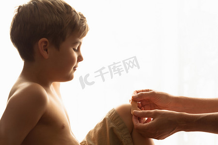 人体白色摄影照片_女人的手把橡皮膏放在儿子的膝盖上