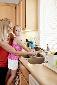 回弹海绵摄影照片_母亲在厨房水槽里给女儿洗手