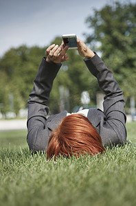 用智能手机拍摄躺在草地上的中年红发妇女的体表图