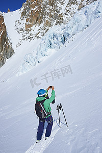 高尔夫球包摄影照片_男性滑雪者在法国格拉尼亚阿尔卑斯山的勃朗峰上用智能手机拍照