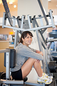 中年女性运动摄影照片_坐在健身房健身器上的女性