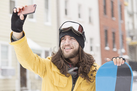 面带微笑的男性滑雪者在街上用智能手机自拍