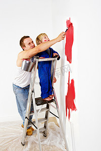男人和蹒跚学步的男孩把墙壁涂成红色