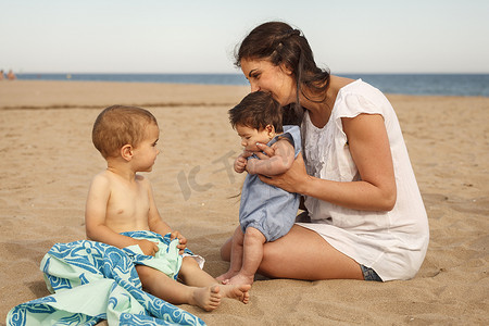 儿童培育摄影照片_坐在海滩上的母亲和婴儿