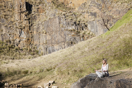 在湖边岩石上做瑜伽姿势的年轻女子