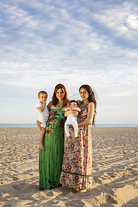 站在海滩上抱着婴儿和蹒跚学步的孩子的母亲