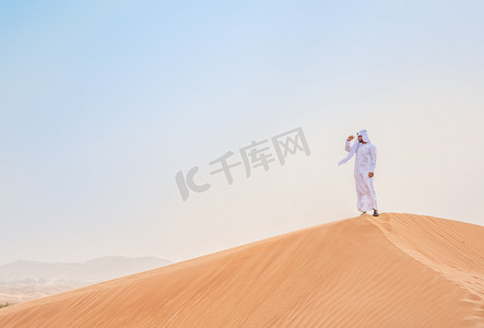 仅限一人摄影照片_阿拉伯联合酋长国迪拜一名身穿传统服装的中东男子从沙漠沙丘向外张望