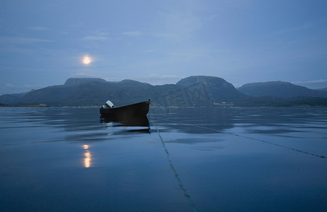 神秘效果摄影照片_夜晚风平浪静的海面上的木船