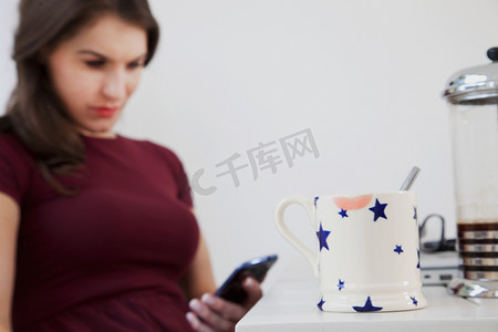 咖啡壶摄影照片_使用手机的年轻女子前景中有咖啡杯