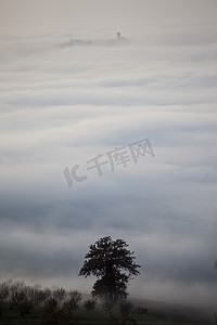 山麓浪河低云中浮现出的树木和屋顶的剪影意大利