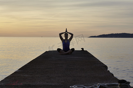 黄昏时分年轻女子坐在码头上做瑜伽姿势