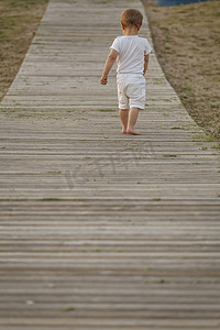 蹒跚学步的孩子走在木板路上的后视线