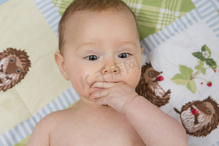 斜上摄影照片_7个月大的女婴躺在婴儿床上手指放在嘴里