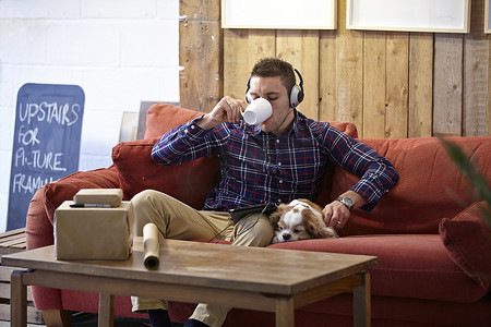 一名中年男子在相框陈列室里喝着咖啡抚摸着狗