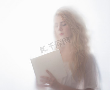 透明纯色摄影照片_年轻女子在磨砂玻璃后看书的模糊镜头