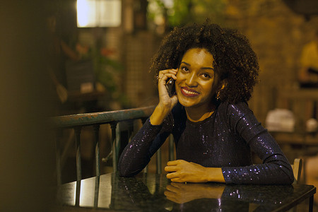 一名年轻女子坐在酒吧的桌子旁用手机