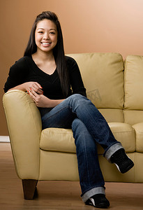 盘腿坐的女孩摄影照片_坐在沙发上微笑的女孩