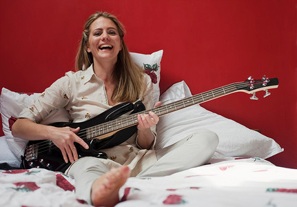 坐弹吉他摄影照片_在床上弹吉他的女人