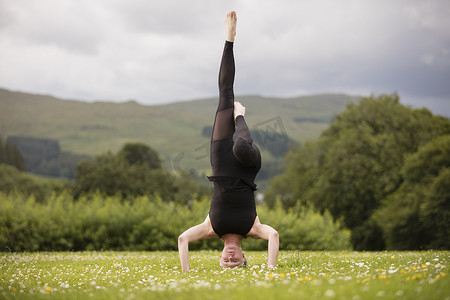 练习瑜伽的成熟女性在田野中抬起腿头朝下站立