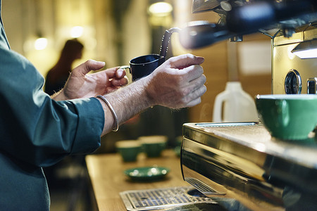 剪影咖啡杯摄影照片_咖啡厅咖啡机上男咖啡师加热牛奶罐的剪影