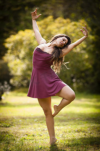身长的中年妇女身着短裙在草地上跳舞一条腿举起手臂