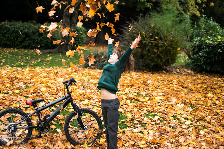 公园里的男孩骑着自行车扔秋叶