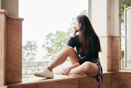 香港维多利亚山废弃房屋的窗台外凝视的年轻女子