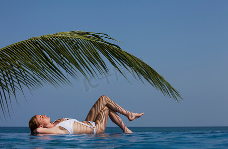 无边泳池旁棕榈叶下的女人