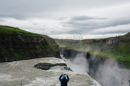 用智能手机拍摄冰岛瀑布的中年妇女的高角后视