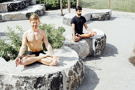 瑜伽运动健身俱摄影照片_两名男子在公园石椅上摆出荷花姿势冥想