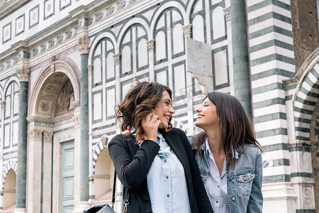 礼拜一摄影照片_意大利托斯卡纳佛罗伦萨圣玛丽亚·诺维拉广场一对使用手机面对面微笑的女同性恋夫妇