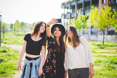 三位年轻女性朋友在公园里摆姿势拍智能手机自拍