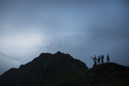 四个年轻的成年男子的剪影手臂举在山顶上