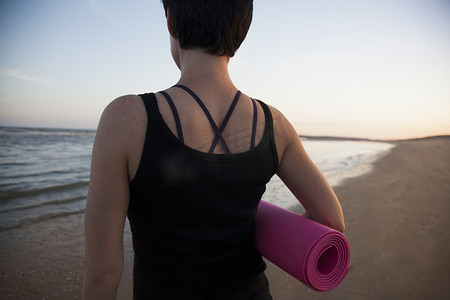 日落时分中年妇女在海滩上准备瑜伽的背影