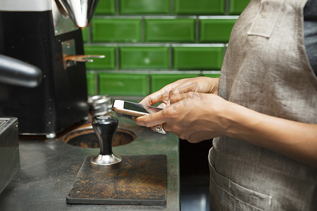 智能造摄影照片_咖啡馆厨房里的女咖啡师用智能手机发短信的中段