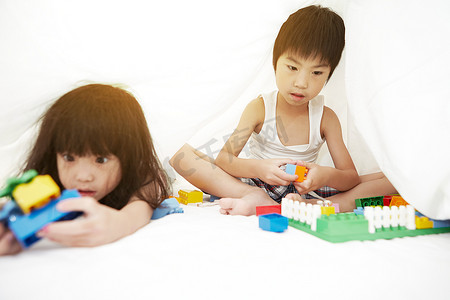 年轻的中国男孩和女孩在床上玩床单下的玩具