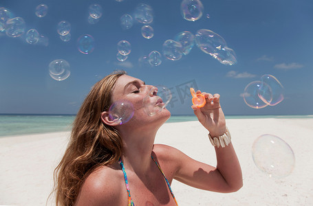 漂浮的泡泡摄影照片_一名女子在海滩上吹泡泡