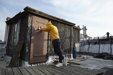 一位年轻男子靠在屋顶的小屋上俯视着