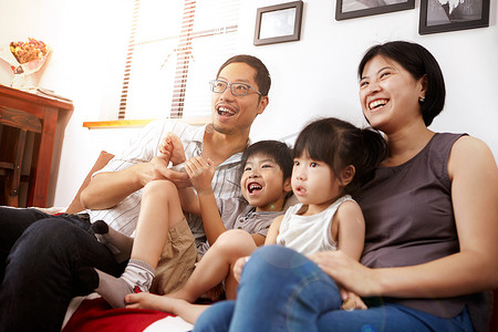年轻的现代中国家庭父母和两个年幼的孩子坐在沙发上一起在家看电视