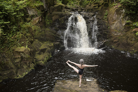 成年女子在瀑布前练习瑜伽的背影