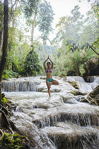 一条腿站立摄影照片_老挝琅勃拉邦广寺瀑布一名女子单腿站立摆出树的姿势